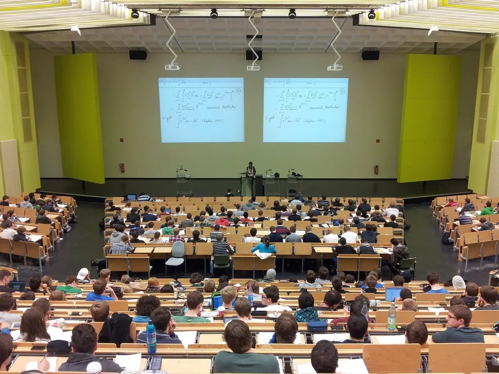 A university lecture hall full of students watching two projected slides.