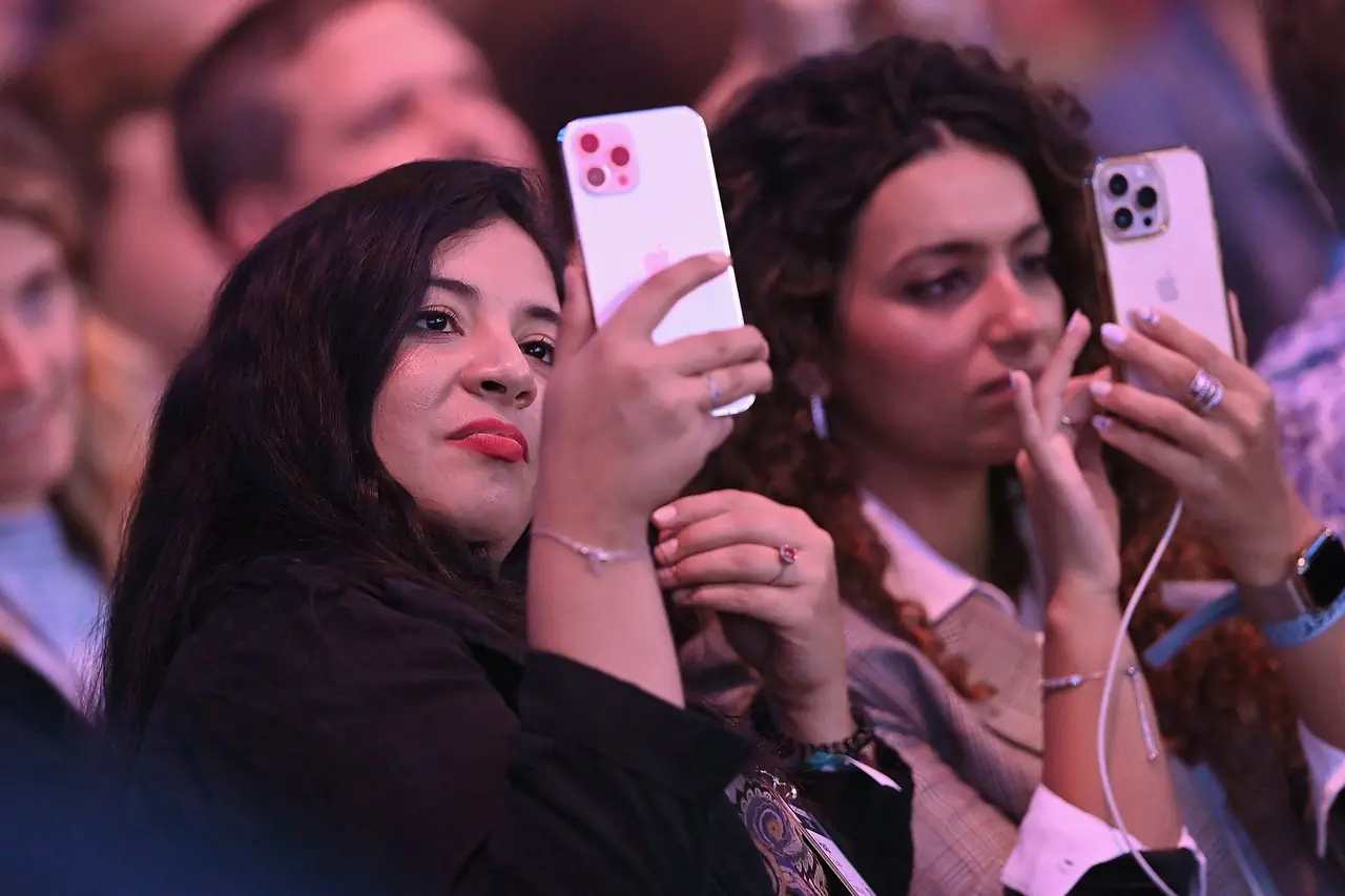 Two women in a conference audience holding up their phones.