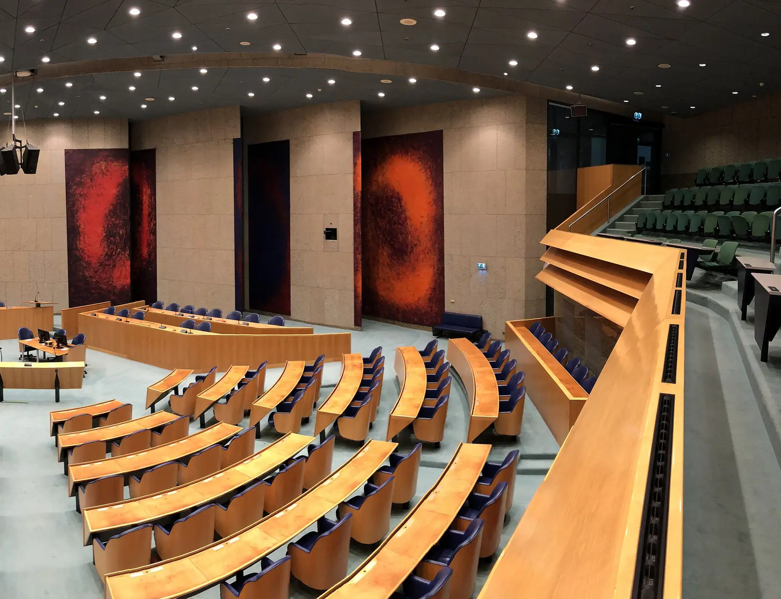 An empty parliamentary plenary hall with curved rows of wooden desks.